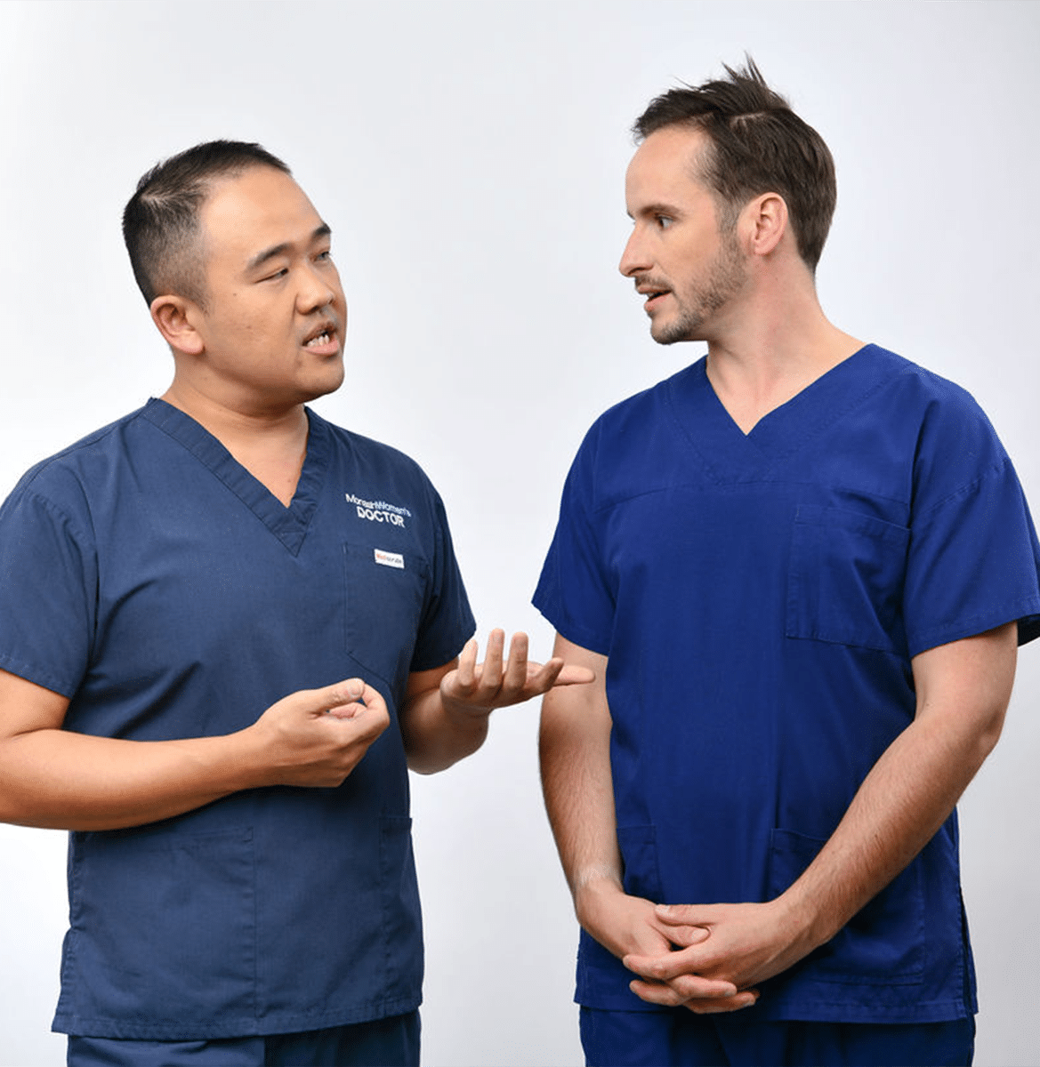 Two clinicians wearing scrubs have a conversation